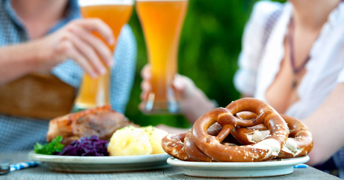 Couple toasting beer glasses at Oktoberfest in Germany with Bavarian pretzels in foreground