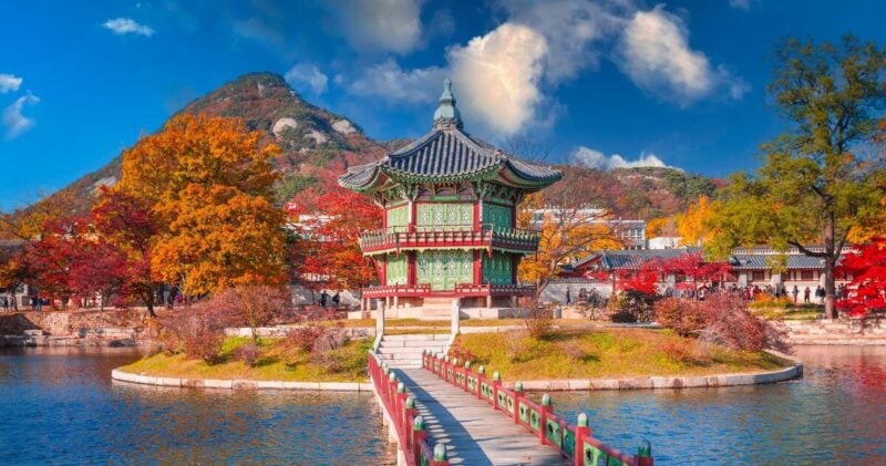 Hyangwonjeong Pavilion at Gyeongbokgung Palace in Seoul, South Korea, surrounded by vibrant autumn foliage and mountains.