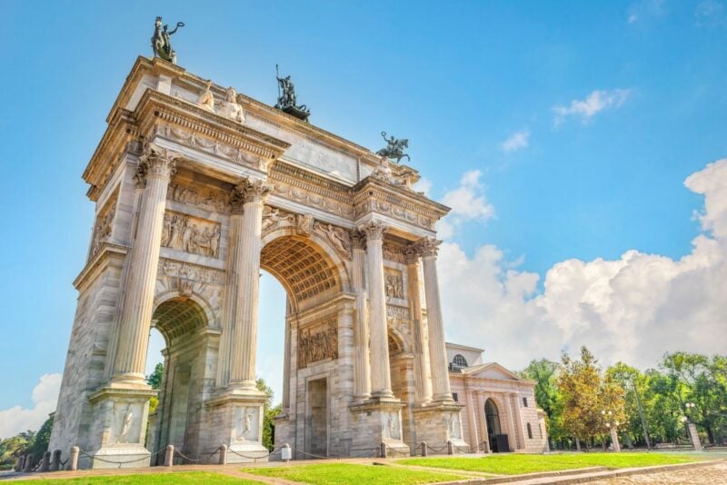 The neoclassical Arch of Peace (Arco della Pace) in Milan, Italy, standing tall against a blue sky, topped with bronze statues of chariots.