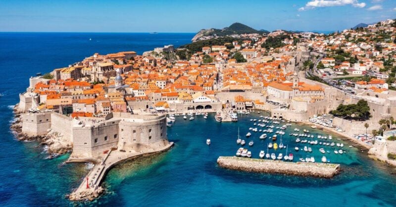 Panoramic landscape of Dubrovnik's walled Old City at the water's edge, showcasing the historic architecture and harbor under a clear blue sky.