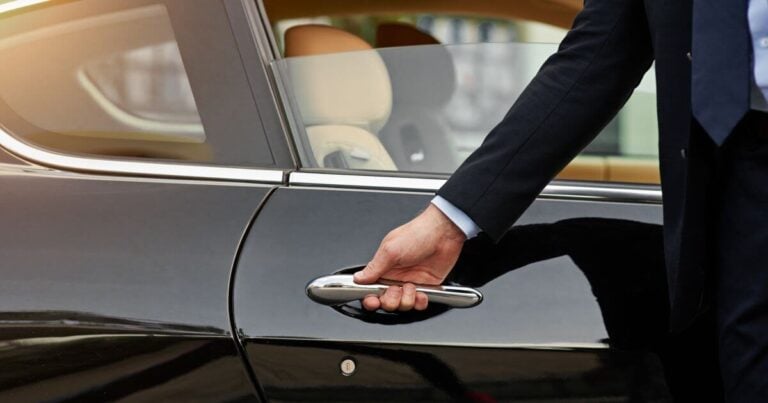 Close-up of a professional chauffeur in a suit opening the door of a black luxury sedan for a passenger.